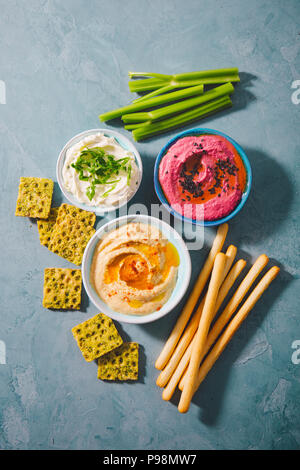 Appetizing vegetarian healthy dips sauces in small bowls with cut vegetables on cutting board. View from above. Healthy detox weight loss concept. Stock Photo