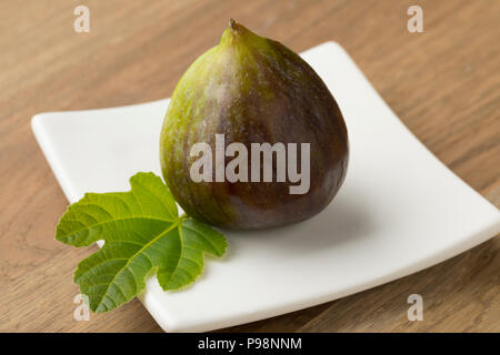 Single fresh ripe fig and a leaf on a dish for dessert Stock Photo