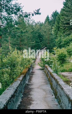 the now-disused concrete of the 1984 Sarajevo Olympic Bobsleigh and Luge Track curves through the forest, covered in graffiti Stock Photo