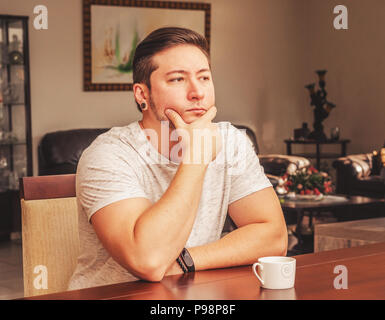 Man seated at home with a serious thoughtful expression. Hand on chin, cup of coffee on the table. Stock Photo