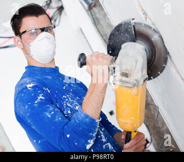 Contractor in mask using professional angle grinder for cutting wall Stock Photo