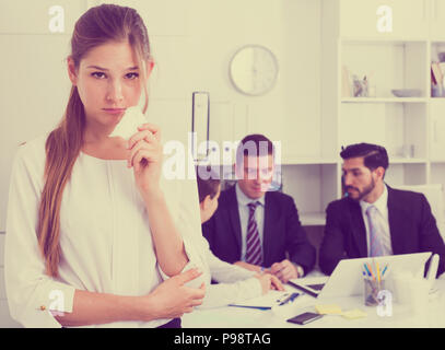Unhappy and crying woman standing at office on background with coworkers Stock Photo