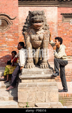 Lalitpur, Kathmandu Valley, Nepal : People next to a guardian  lion statue of the ancient royal palace at the Unesco listed Patan Durbar square. Stock Photo