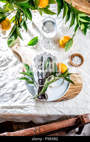 Table setting with white plate, cutlery, linen napkin and orange tree branch decoration on white linen tablecloth . Close up. Table with table setting and shair Stock Photo