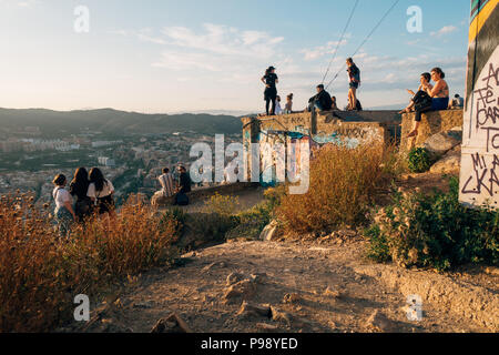 a young group of tourists sit atop Bunquers del Carmel at sunset, a famous lookout over the city of Barcelona, Spain Stock Photo