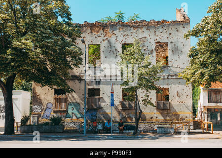 Two locals sit in front of the remains of a artillery shell-ridden building facade, in Mostar, Bosnia and Herzegovina Stock Photo