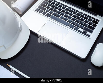 flat lay white hard Safety helmet with laptop, computer mouse control, paper and pencil for engineering worker on black background top view with space Stock Photo