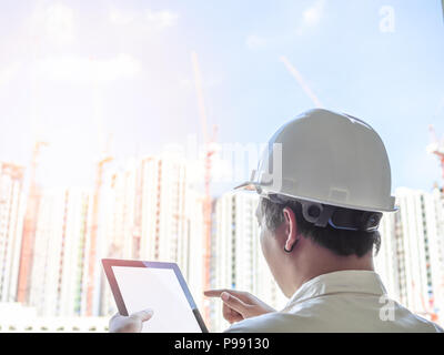 Engineer man back view wearing white hard safety helmet and white shirt touching tablet on his hand for business work on construction building backgro Stock Photo