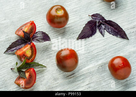 Fresh red cherry tomatoes with basil on a rustic wooden background, selective focus. Stock Photo