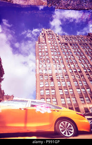 Distorted view of New York City yellow taxi reflected in a puddle, color toned picture, USA. Stock Photo