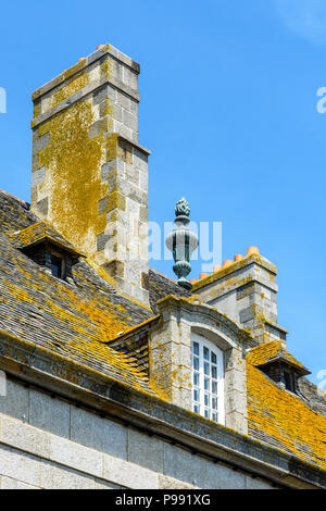 The slate roof covered with lichen, the dormer windows and chimneys of a residential building in the old city of Saint-Malo, France, against blue sky. Stock Photo