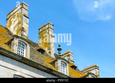 The slate roof covered with lichen, the dormer windows and chimneys of a residential building in the old city of Saint-Malo, France, against blue sky. Stock Photo