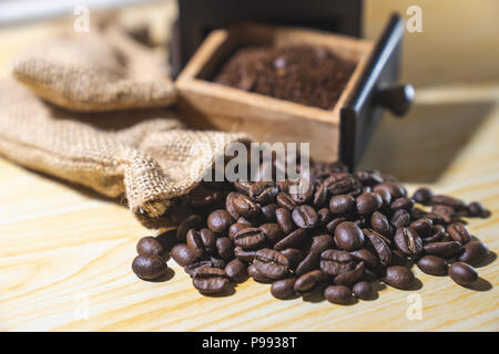 close up roasted coffee beans on wooden background with blured vintage grinder and sack in background Stock Photo