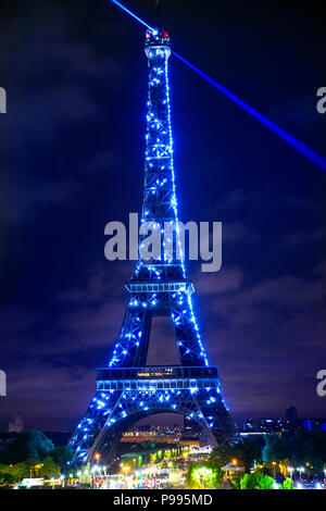 Paris, France - July 1, 2017: blue laser lights from the top of Eiffel Tower shining at night. Eiffel Tower is a symbol of Paris. Vertical shot from Jardins du Trocadero. Stock Photo
