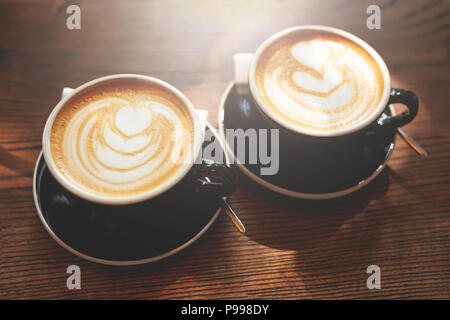 Two cups of cappuccino with latte art on wooden table. Close up. Stock Photo