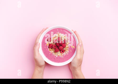 Woman's hands holding raspberries smoothie bowl on pink background. Top view, copy space. Stock Photo