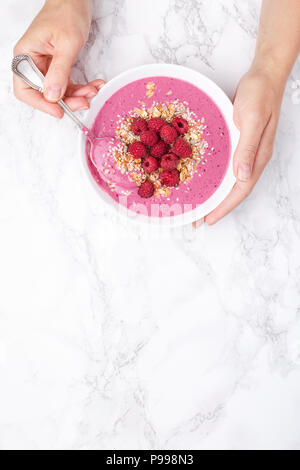 Woman's hands holding raspberries smoothie bowl on marble background. Top view, copy space. Stock Photo