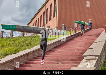 Polotsk, Belarus - July 6, 2018: Oarsmen walk upstairs with canoe on shoulders after rowing training. Stock Photo