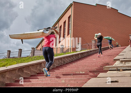 Polotsk, Belarus - July 6, 2018: Athletes walk upstairs with kayaks on shoulders after rowing training. Stock Photo