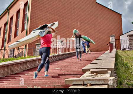 Polotsk, Belarus - July 6, 2018: Teenagers come back to building of sports section after rowing training, they rise up an abrupt ladder, bearing canoe Stock Photo