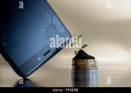 Broken phone display and golden and silver coins in soil with young plant. Repair phones business concept Stock Photo