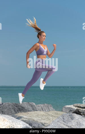 sportswoman running across rocks at the coast, keeping fit outdoors. Stock Photo
