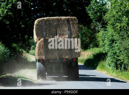 A tractor pulling a load of straw bales blowing up dust on a country road, Warwickshire, UK Stock Photo