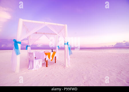 Romantic dinner table set-up for a honeymoon couple on the beach under sunset sky. Exotic wedding and honeymoon concept Stock Photo