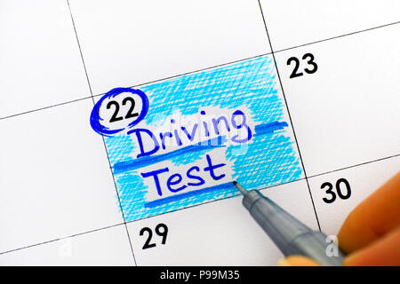 Woman fingers with pen writing reminder Driving Test in calendar. Close-up. Stock Photo