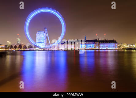 Long exposure night time view of the Coca-Cola London Eye and County Hall from Embankment, London, reflected in the Thames, lit up against a clear sky Stock Photo