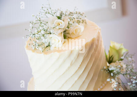 Wedding cake covered in cream butter icing decorated with real flowers and greenery Stock Photo