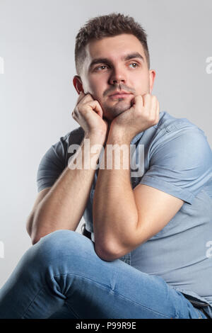 Handsome man sit touching chin look away and thinking. Actors portfolio picture, emotion and feelings. Studio shot, isolated on gray background Stock Photo