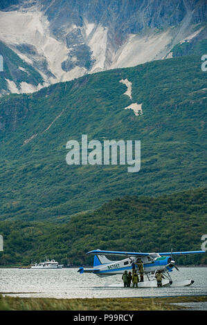 Adventure travelers in Alaska depart from a sea plane in Geographic Harbor, Katmai National Park, Alaska.  Mountainside ash from the Novarupta Volcano Stock Photo