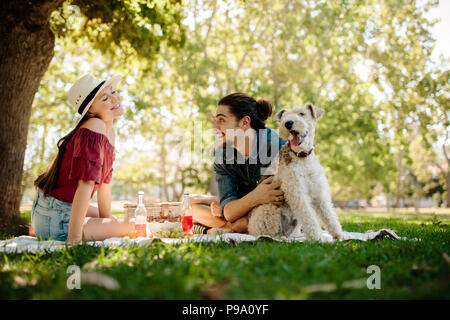 Young man caresses a dog with woman sitting by at city park. Couple having fun on picnic. Stock Photo