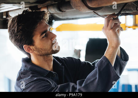 Close up of young car technician checking the electrical wires under the car. Mechanic repairing the car in auto repair shop. Stock Photo