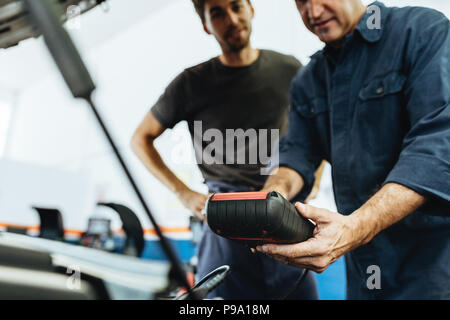 Automobile mechanics holding a device for checking engine condition. Mechanics diagnosing a car engine with device in service station. Stock Photo