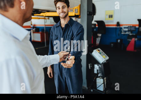 Mechanic receiving car keys from customer in automobile service center. Customer giving his car keys to mechanic at the repair garage. Stock Photo