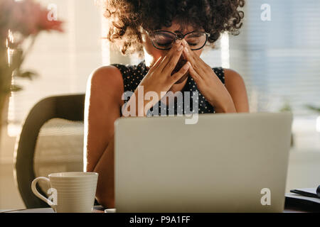Young african businesswoman sitting at her desk looking stressed. Woman having stress on her job. Stock Photo