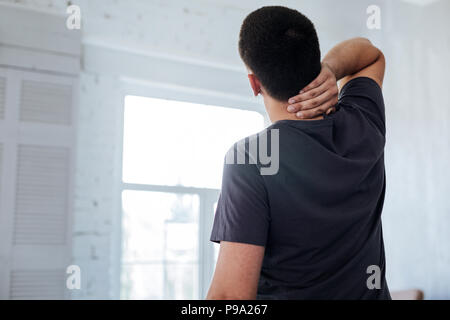 Dark-haired man holding his neck Stock Photo