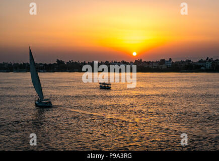 Colourful sunset over the Nile River with silhouettes of river boat and traditional felucca sailing boat, Luxor, Egypt, Africa Stock Photo