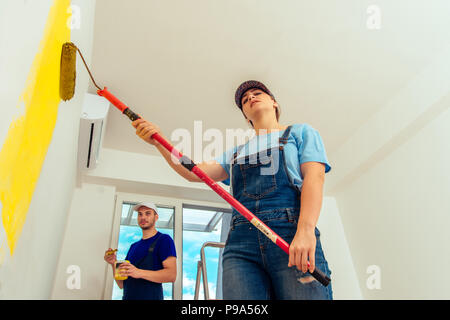 Couple decorating room using paint rollers and paintbrush on wall Stock Photo