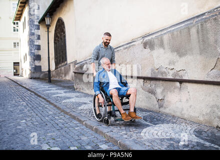 An adult son with senior father in wheelchair on a walk in town.