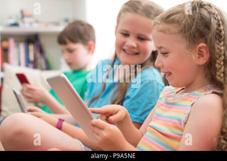 Three Children On Sofa At Home Playing With Digital Devices Stock Photo