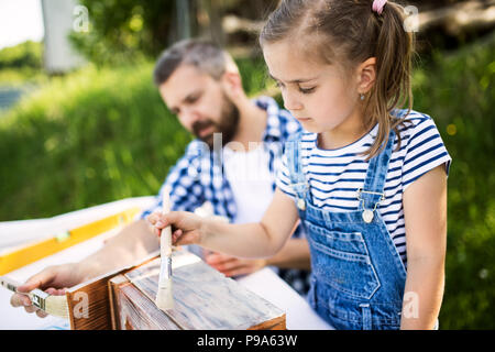 Father with a small daughter outside, painting wooden birdhouse. Stock Photo