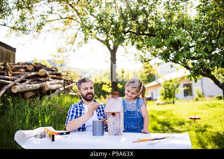 Father with a small daughter outside, painting wooden birdhouse. Stock Photo