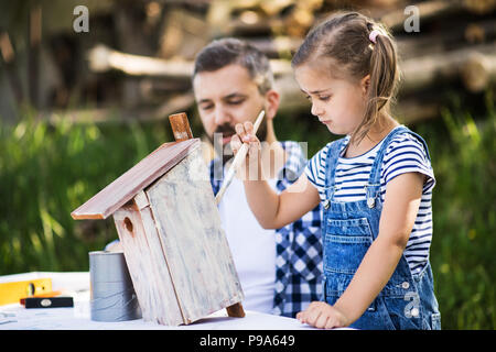 Father with a small daughter outside, painting wooden birdhouse. Stock Photo