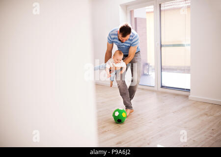 Young father with a baby son at home playing with a ball. Stock Photo