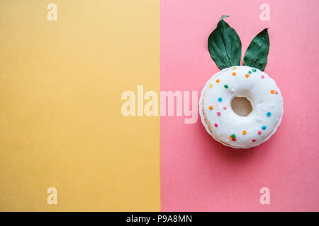 A creative donut with ears of leaves resembling a rabbit on a colored background in a minimal style. Stock Photo