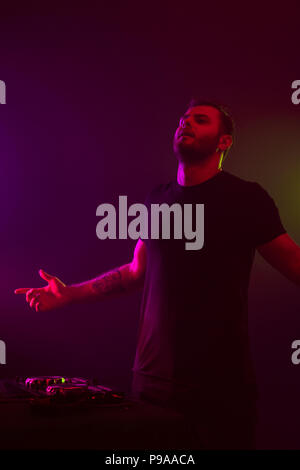 Attractive young DJ playing on turntables with color light effects Stock Photo