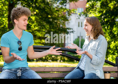 A guy with a girl in summer in a park in nature. Emotionally communicates with gestures. Smiles happily. Camping. Dressed in casual clothes. Stock Photo